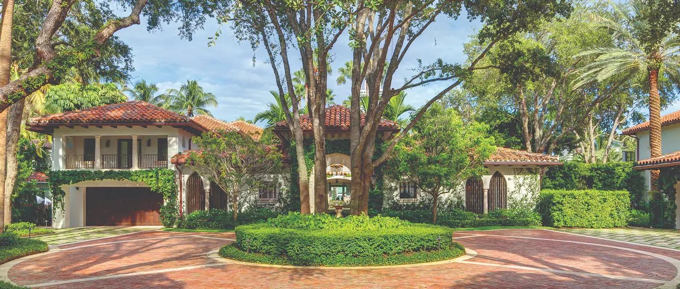 Approach view of the Spanish-style main house from the circular driveway, framed by mature palms.