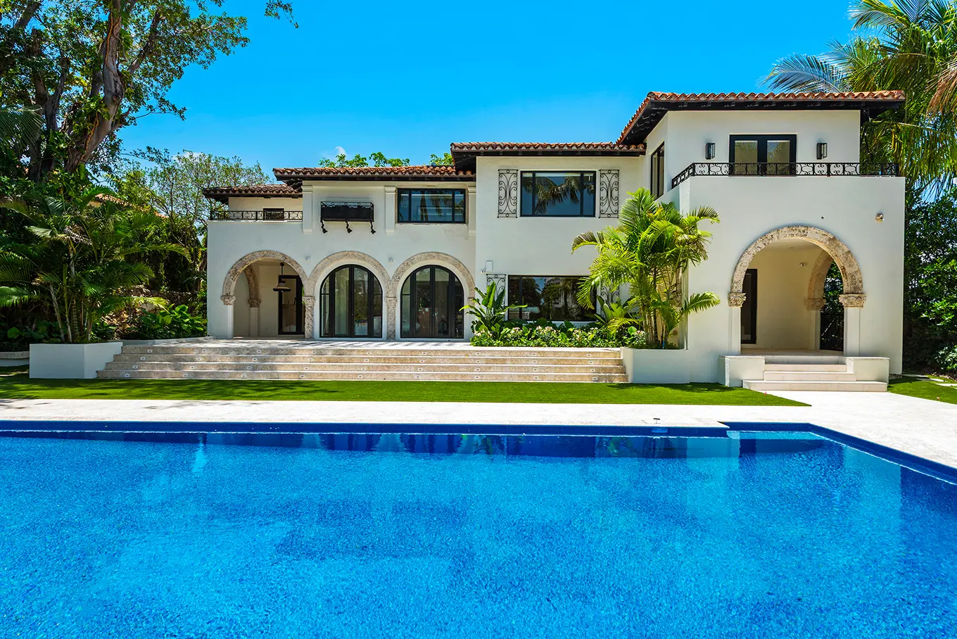Spanish Mediterranean estate with classic arched colonnade, terracotta tile roof, and stunning infinity pool surrounded by tropical landscaping
