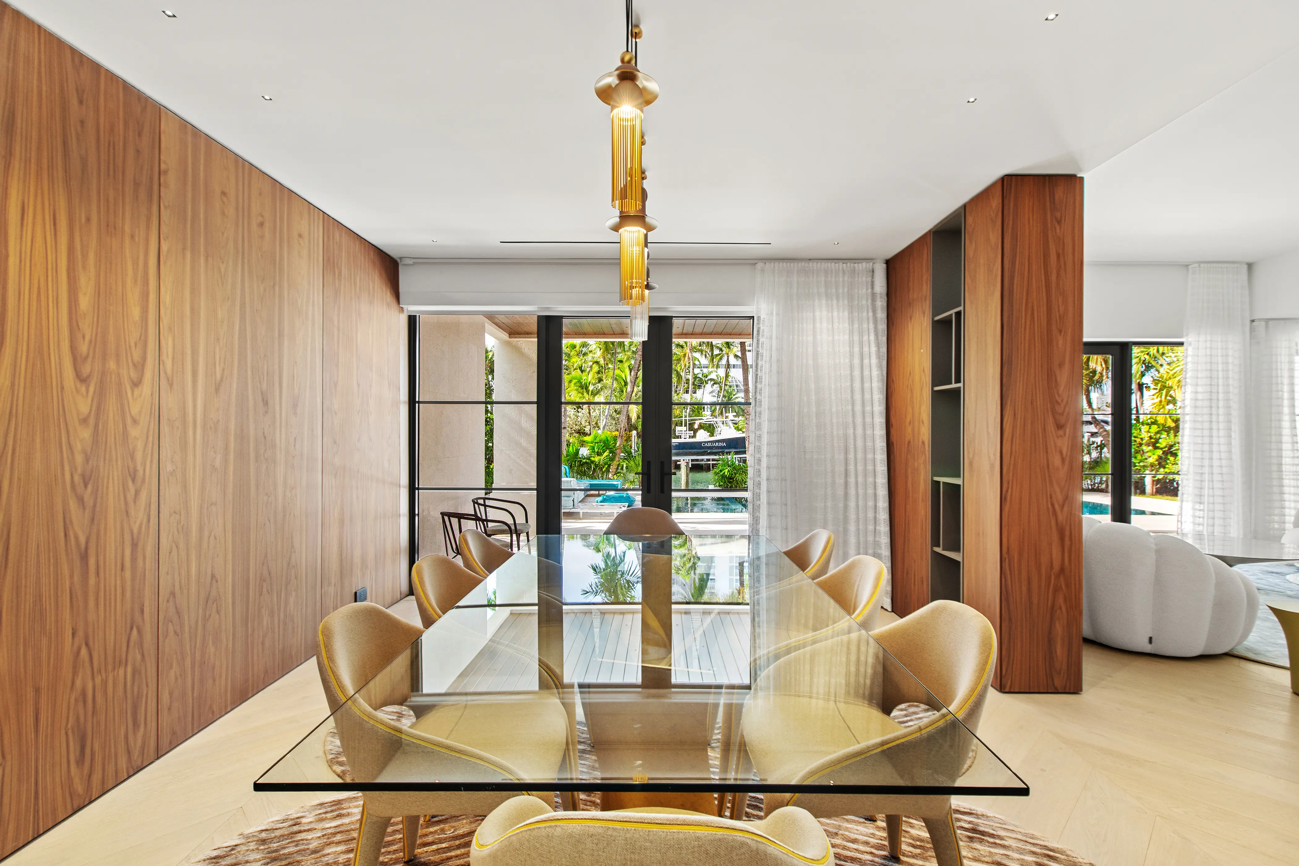 Contemporary dining space featuring custom floor-to-ceiling wood millwork, a glass dining table, statement lighting, and seamless indoor-outdoor living.