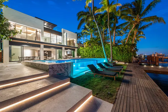 Glass-walled infinity pool illuminated at night, overlooking the bay and a large modern dock.