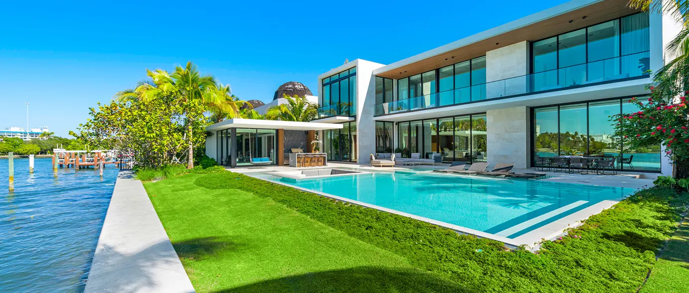 Bay-side view of the pool and house, showcasing expansive walls of glass.