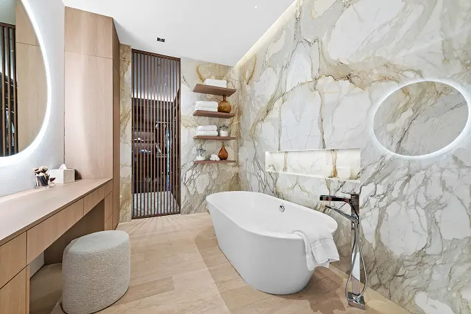 Modern bathroom with white marble walls, wood flooring, and a sculptural soaking tub.