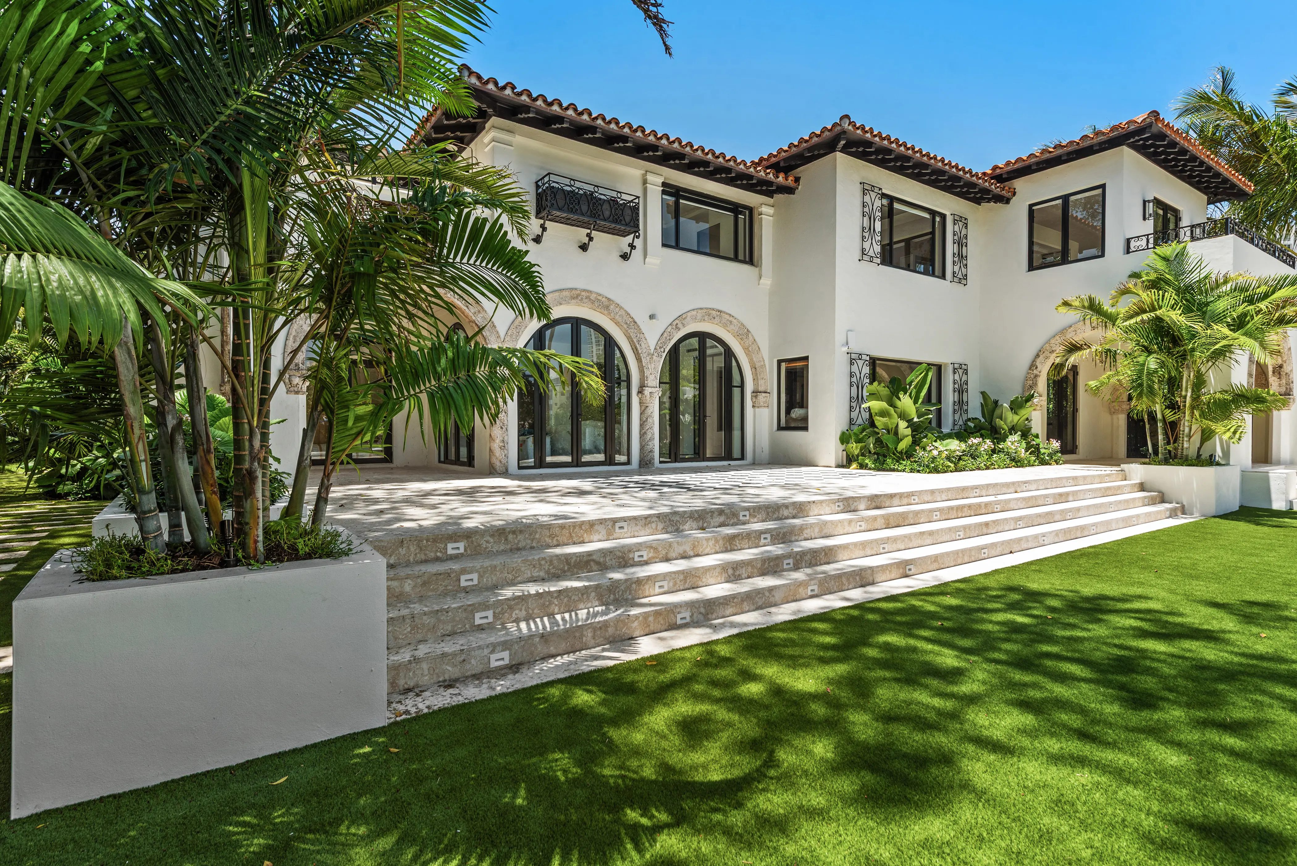 Spanish Mediterranean estate with white arched poolside pavilion, vibrant blue pool, and lush tropical gardens in Miami
