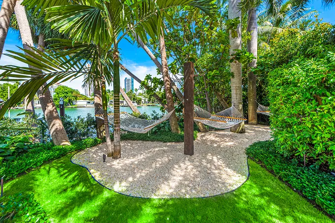 Tranquil waterside garden with a hammock lounge nestled among swaying palm trees.