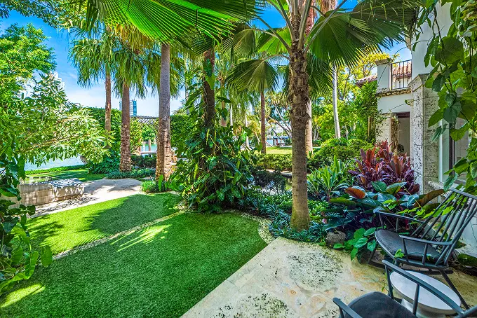 Lush waterside garden bursting with tropical plants and mature trees along the property's edge.