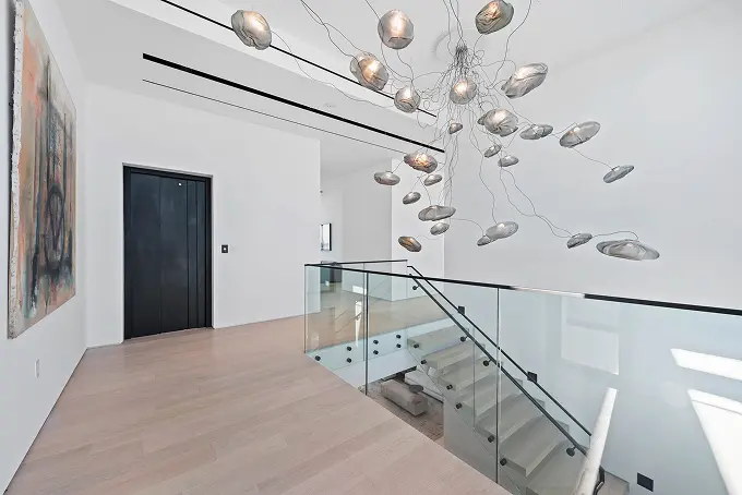 View from the top of the staircase, featuring a glass railing and a modern abstract chandelier.