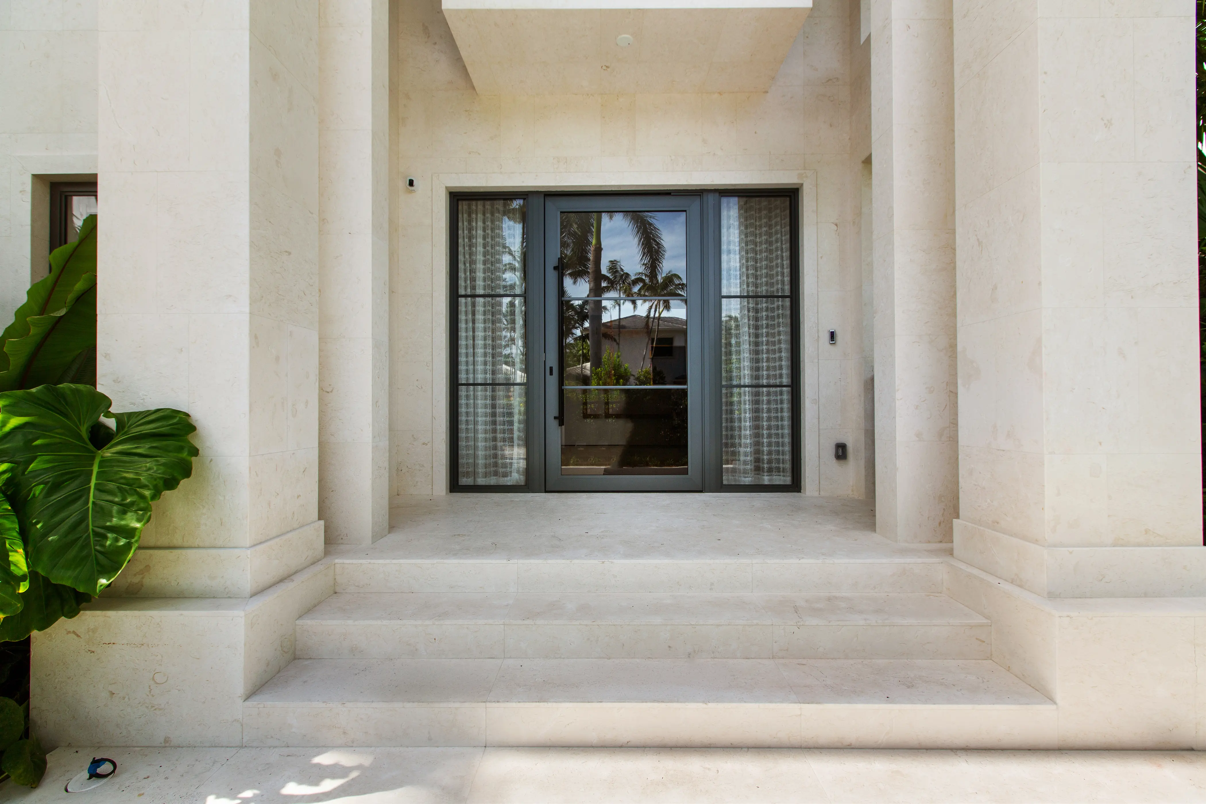 Elegant residential entryway featuring natural stone walls, architectural columns, limestone flooring, and custom black-framed glass doors.
