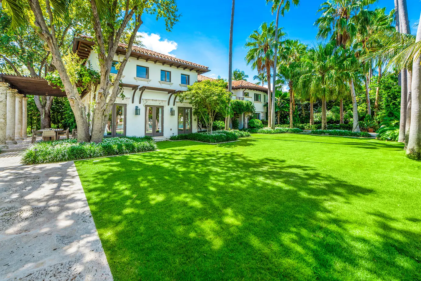 Sweeping front lawn lined with palm trees leading up to the Spanish-style estate.
