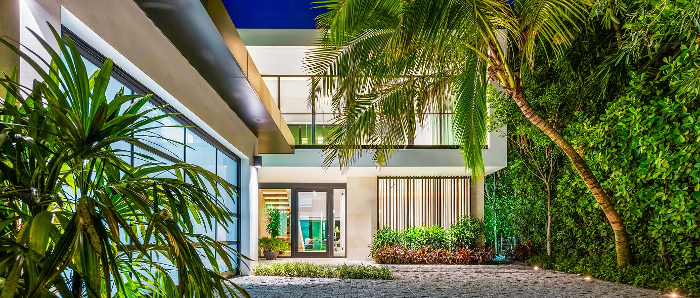 Illuminated modern driveway courtyard framed by palms and lush living walls.