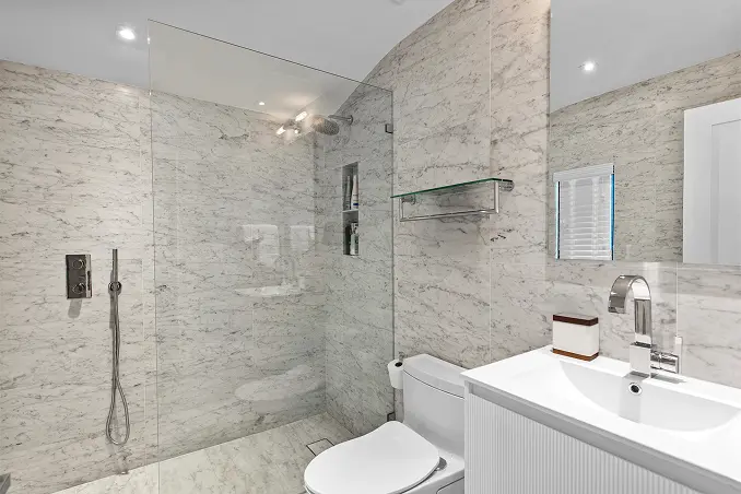 Bright bathroom featuring a spacious walk-in shower enclosed by floor-to-ceiling marble walls.