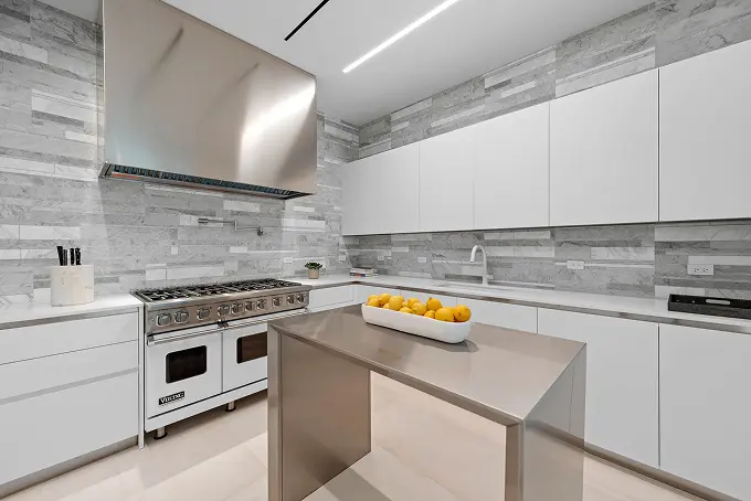Modern white kitchen with tall ceilings and a striking stone backsplash.