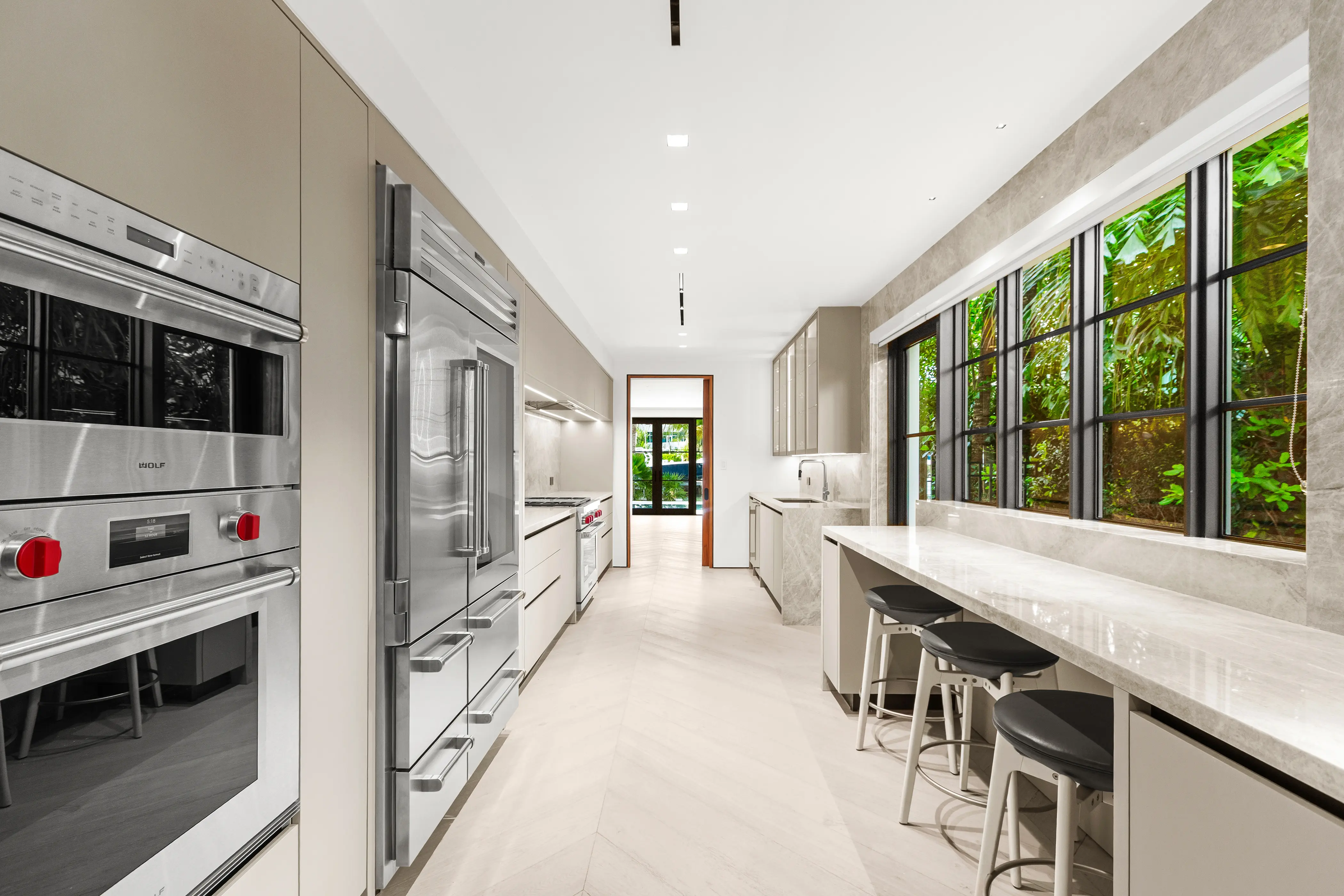 Sleek contemporary kitchen featuring custom cabinetry, marble countertops, integrated appliances, counter seating, and abundant natural light.
