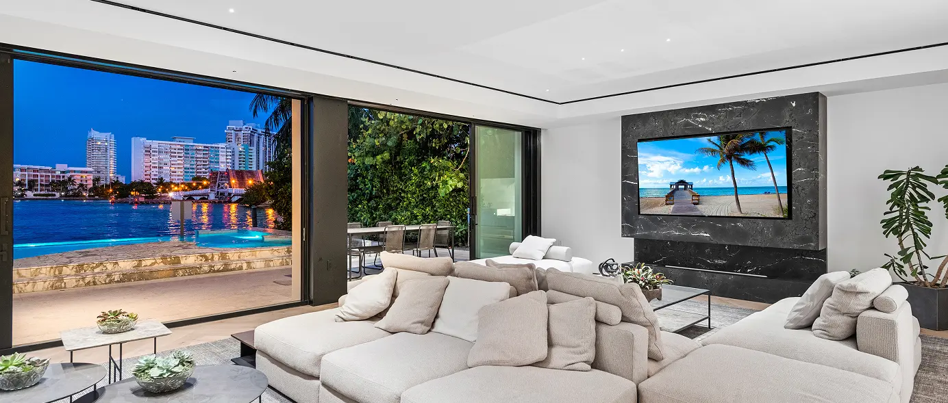 Spacious living room opening through large sliding glass doors to the pool and bay beyond.