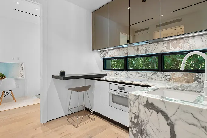 Bright white marble kitchenette with soaring ceilings and sleek glass-front cabinets.