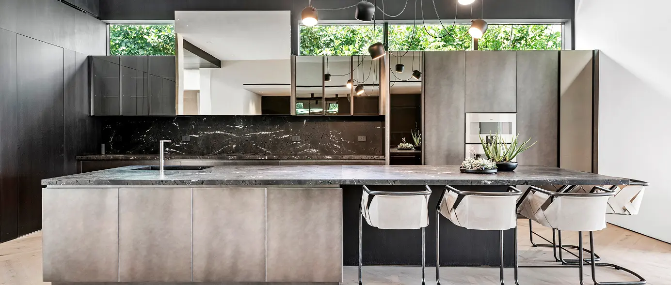 Brutalist-inspired kitchen blending raw concrete and black marble with a large island under tall ceilings.