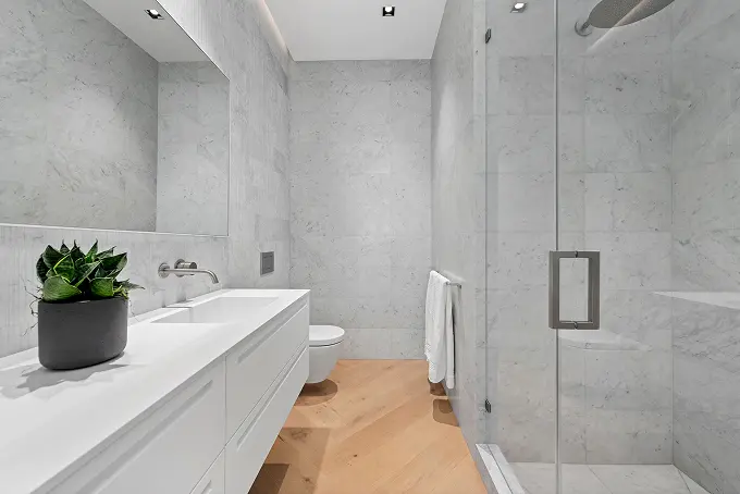 Elegant white stone bathroom with a tall walk-in shower and warm wood flooring.