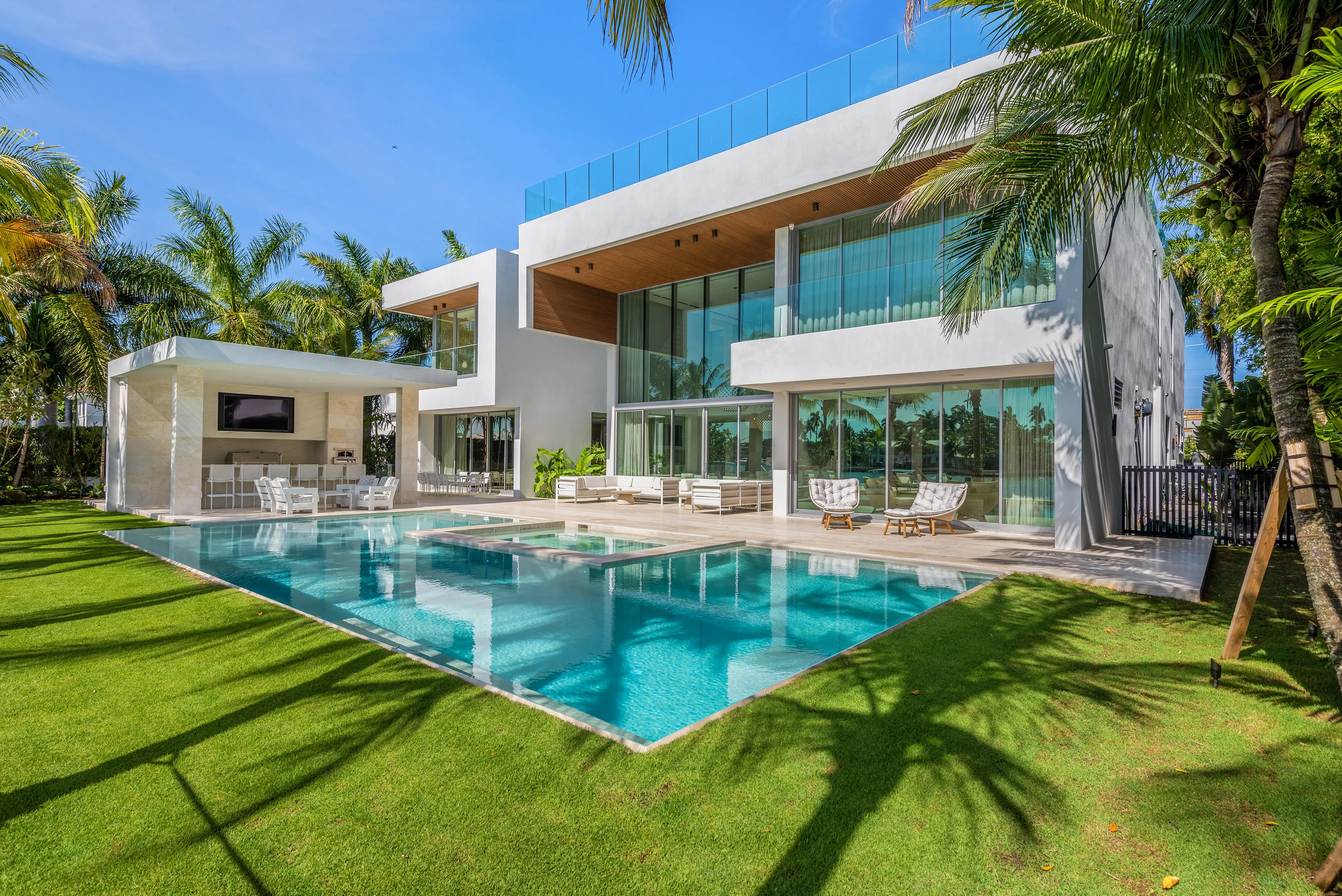 Sleek modern residence with an expansive pool, manicured lawn, and tropical palm landscaping under bright Miami skies
