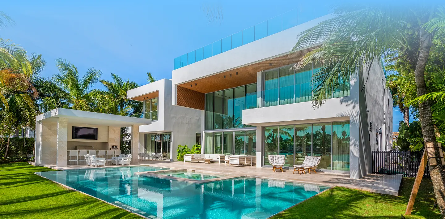 Sleek modern residence with an expansive pool, manicured lawn, and tropical palm landscaping under bright Miami skies