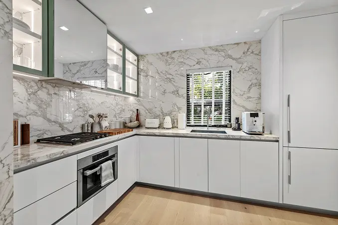 Bright kitchen with a dramatic white and grey marble backsplash beneath soaring ceilings.