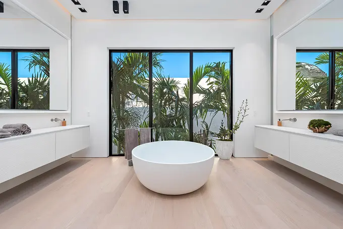 Spacious modern bathroom with a soaking tub overlooking swaying palm trees.