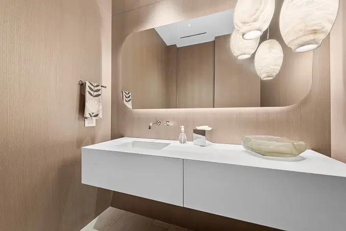 Modern bathroom featuring warm wood walls and a sleek backlit mirror.