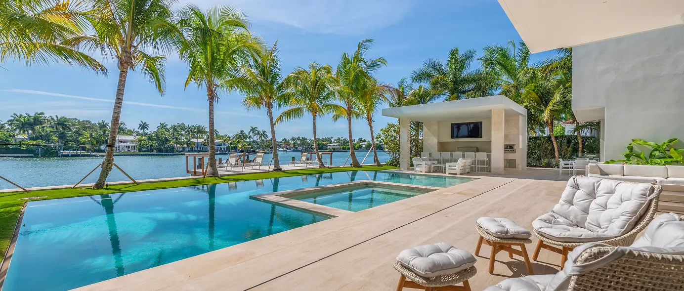 Patio view overlooking the pool, hot tub, palm trees, and the lake beyond.