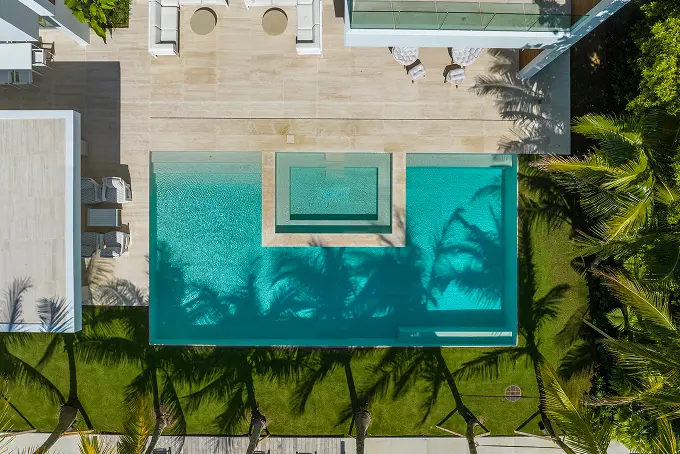 Aerial view of the pool framed by a palm-lined lawn and white wood patio decking.