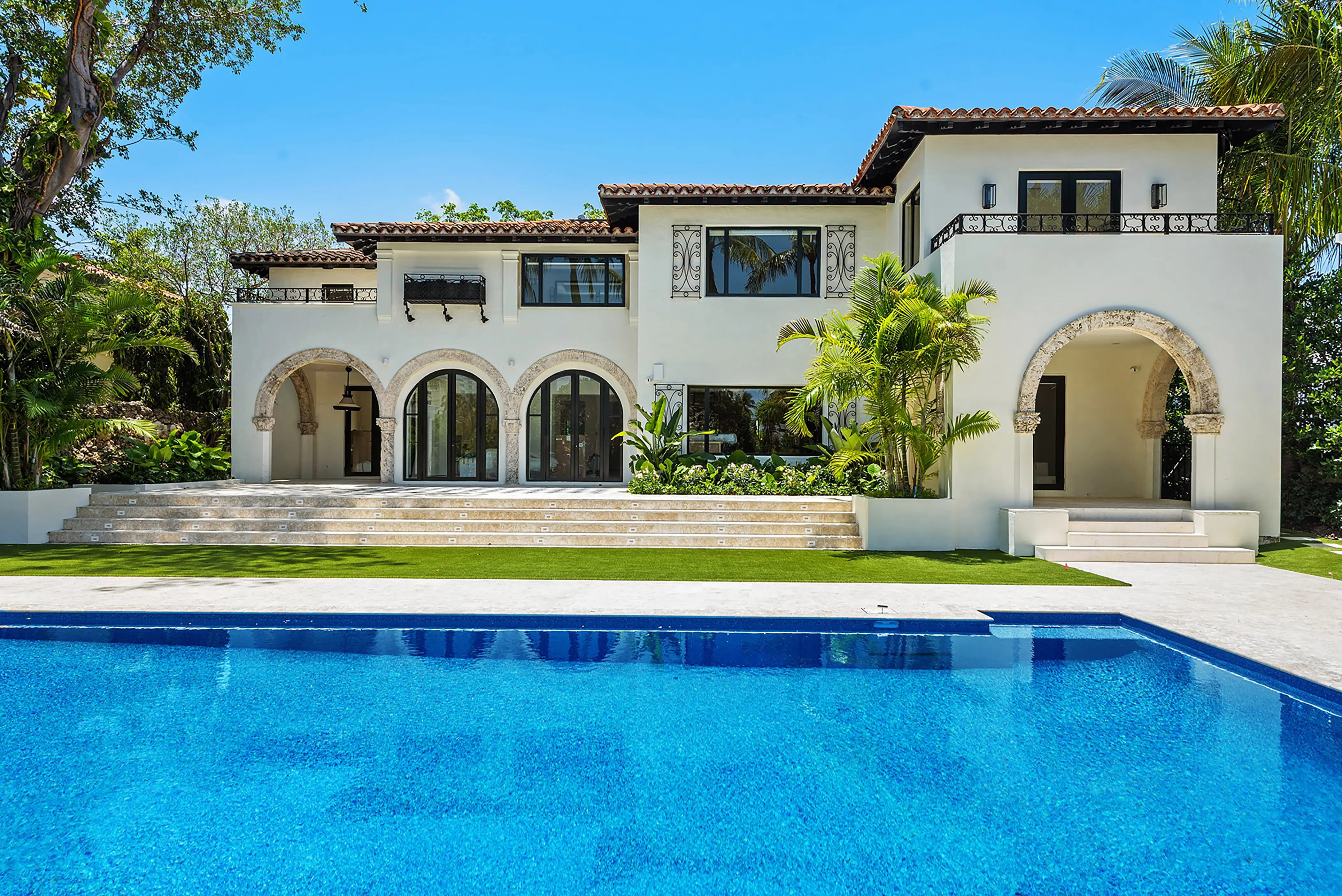 Spanish Mediterranean estate with classic arched colonnade, terracotta tile roof, and stunning infinity pool surrounded by tropical landscaping