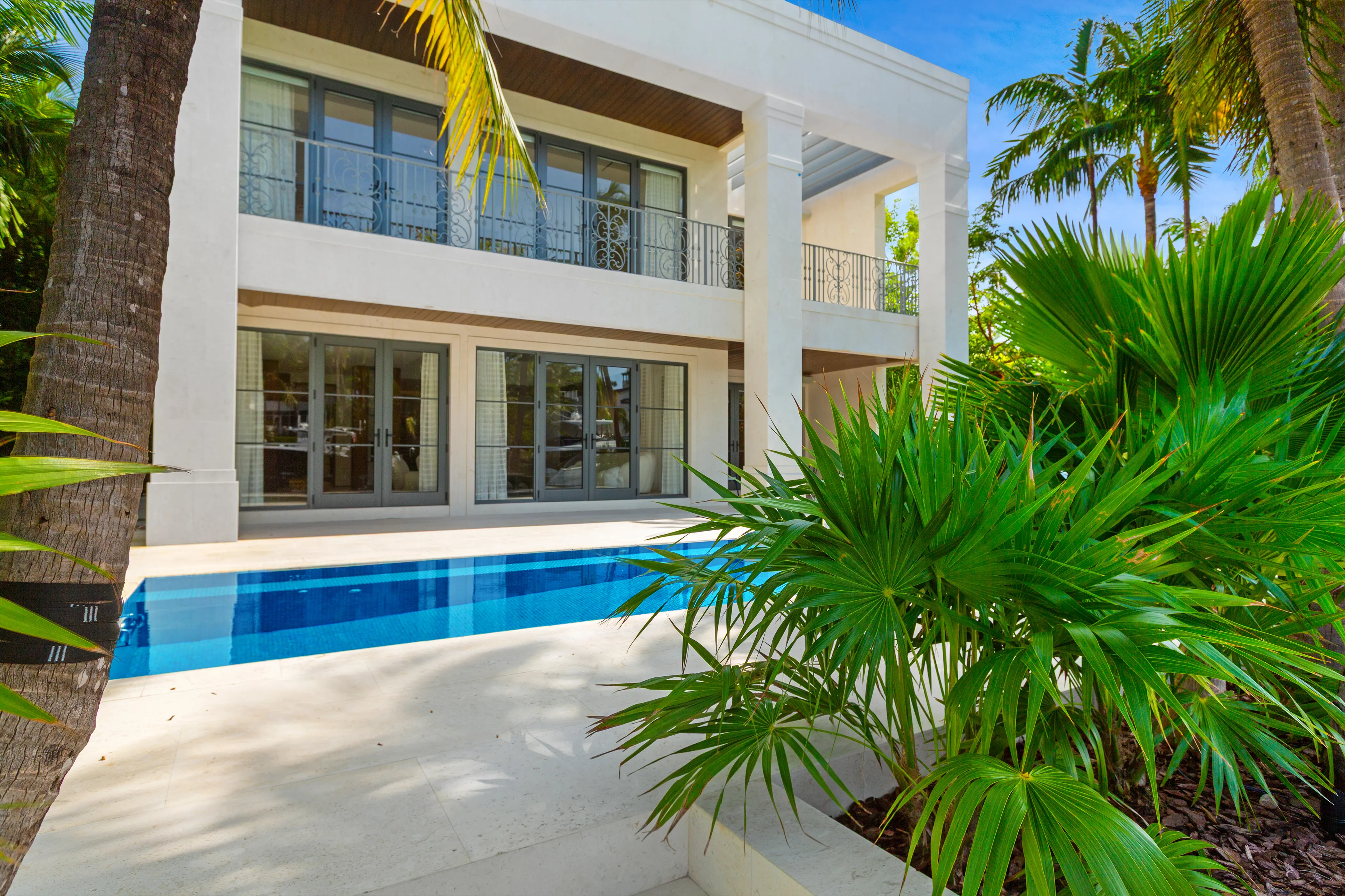 Contemporary Miami Beach residence opening onto a private swimming pool surrounded by lush tropical landscaping and seamless indoor-outdoor living areas.
