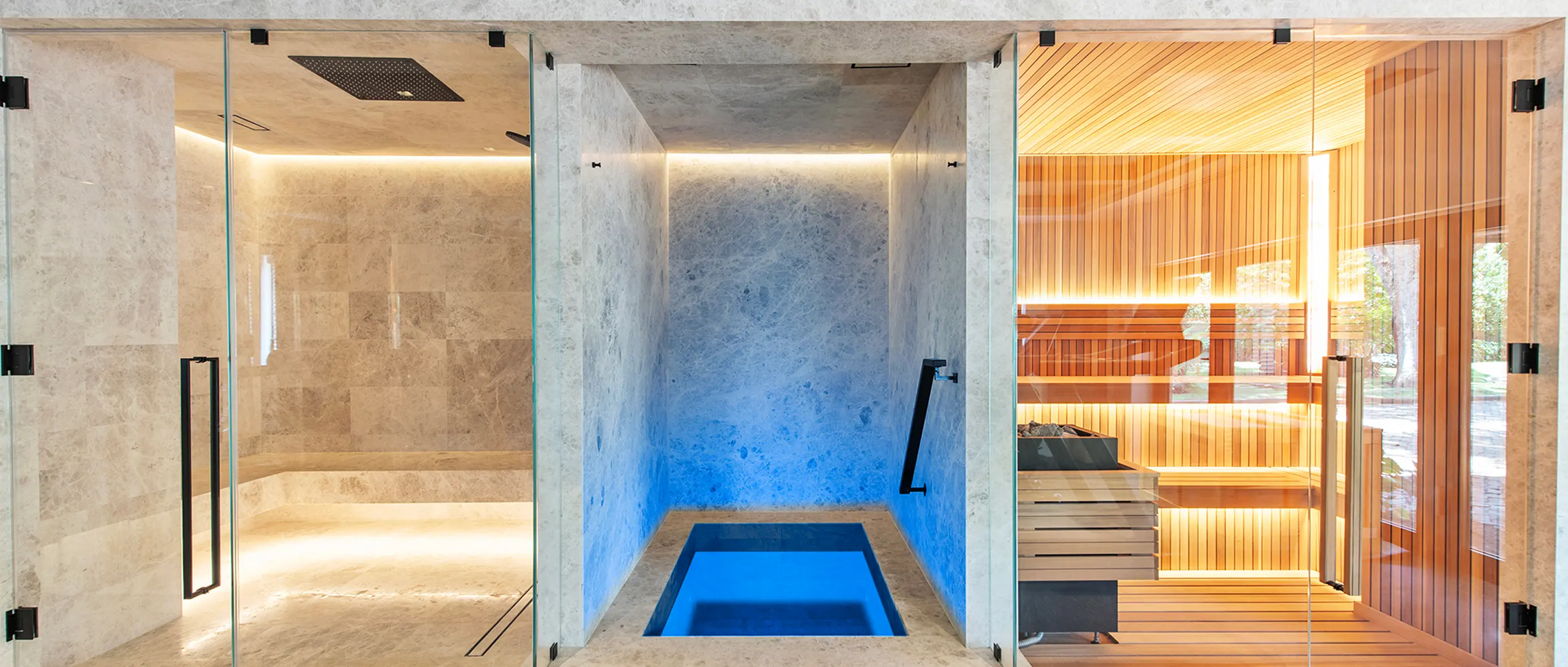 Luxury spa bathhouse featuring marble steam shower, blue-lit cold plunge pool, and cedar wood sauna