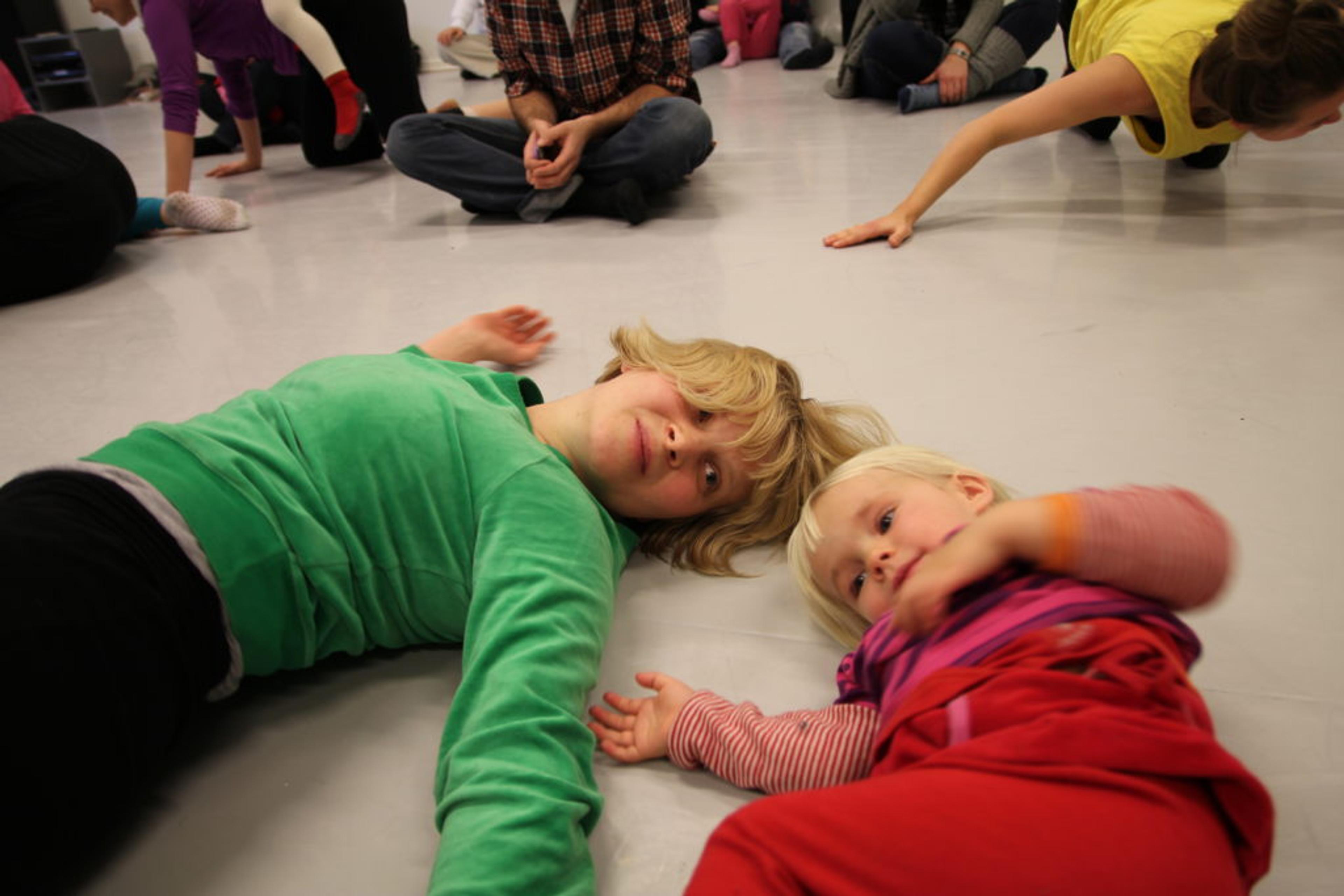 Et barn med grønn genser ligger på gulvet ved siden av et annet barn med rød genser.