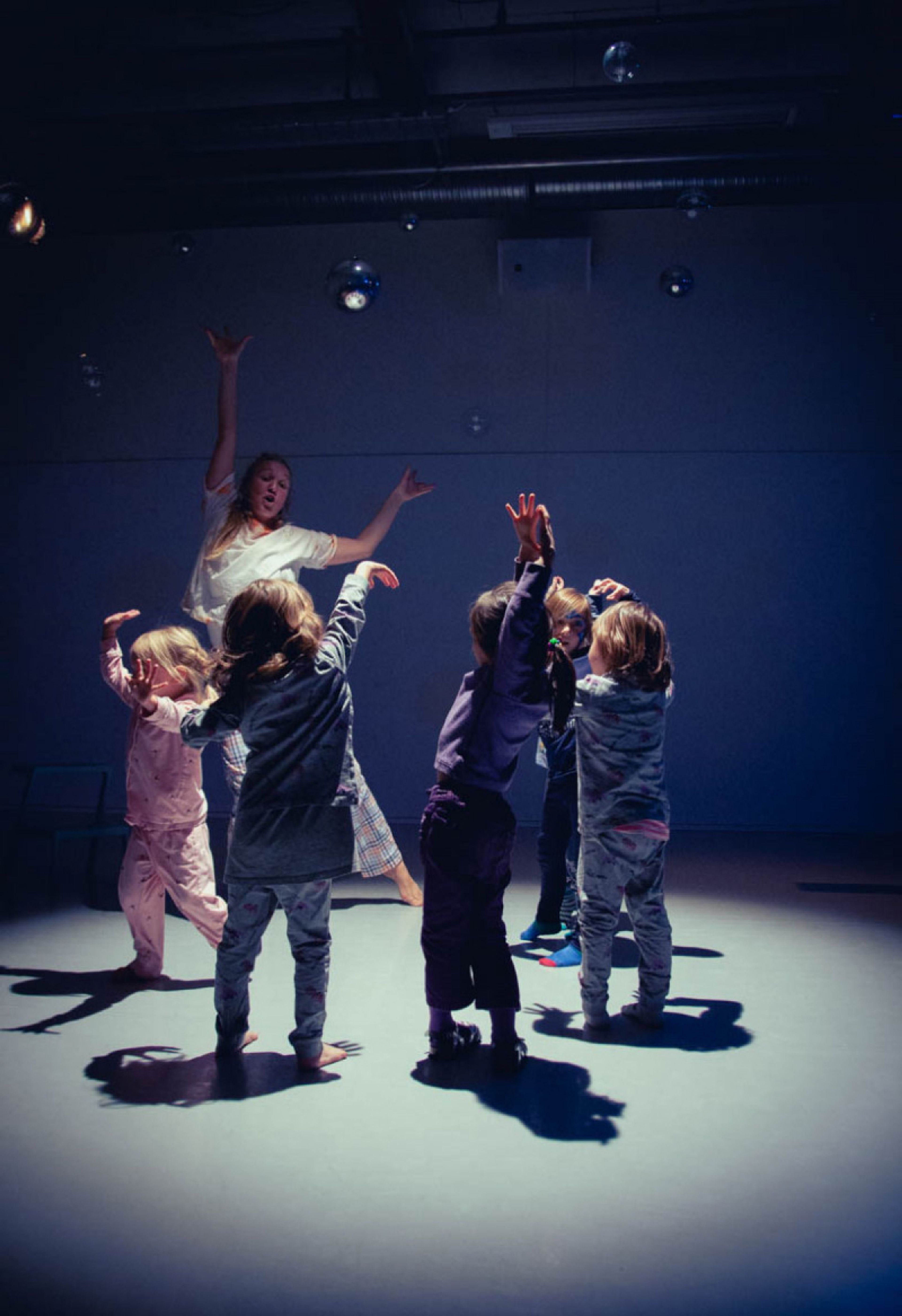 Barn danser i ring på en scene, med en voksen. Foto. 