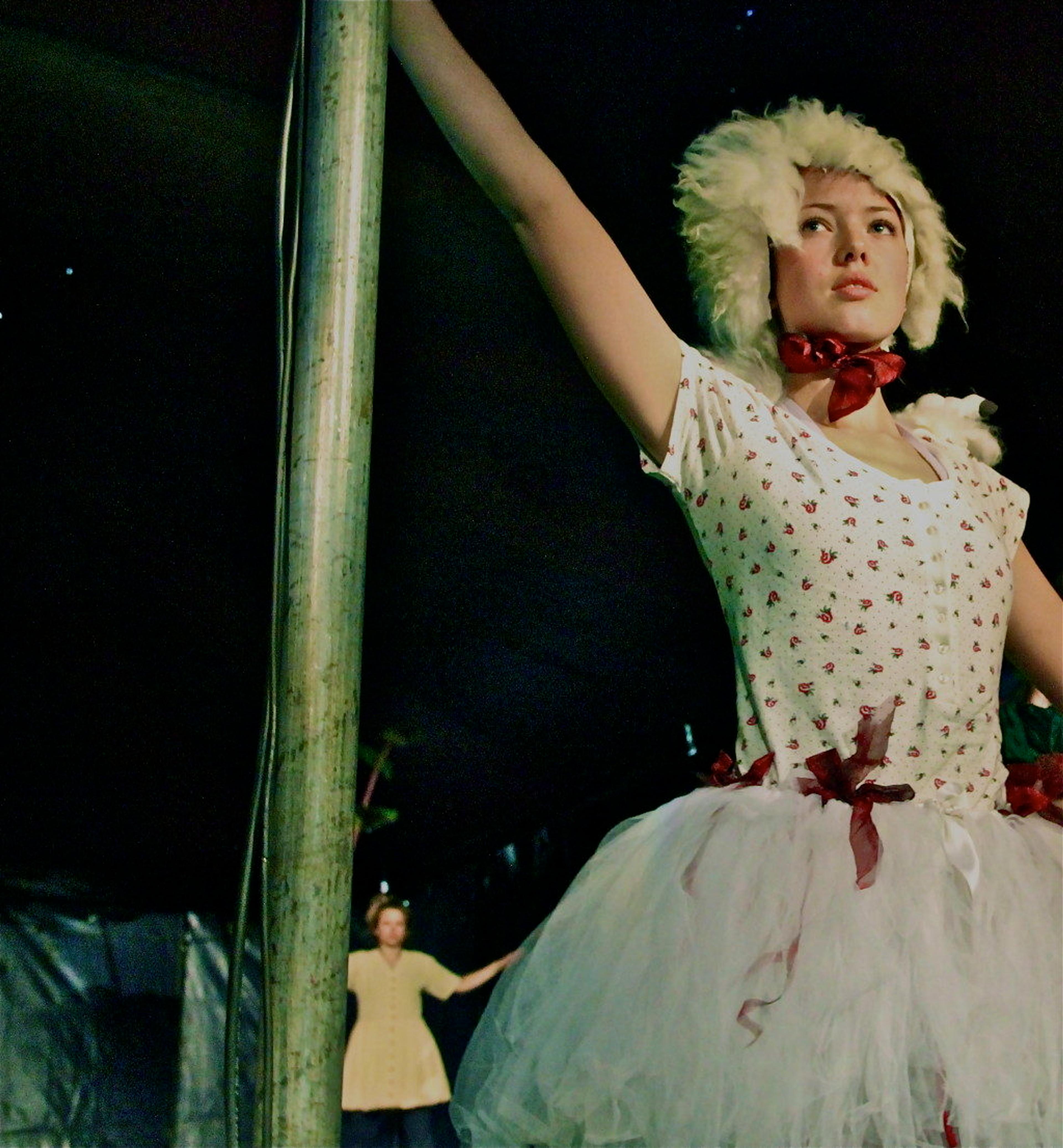 En dame danser ikledd hvit parykk og hvit kjole med røde prikker.