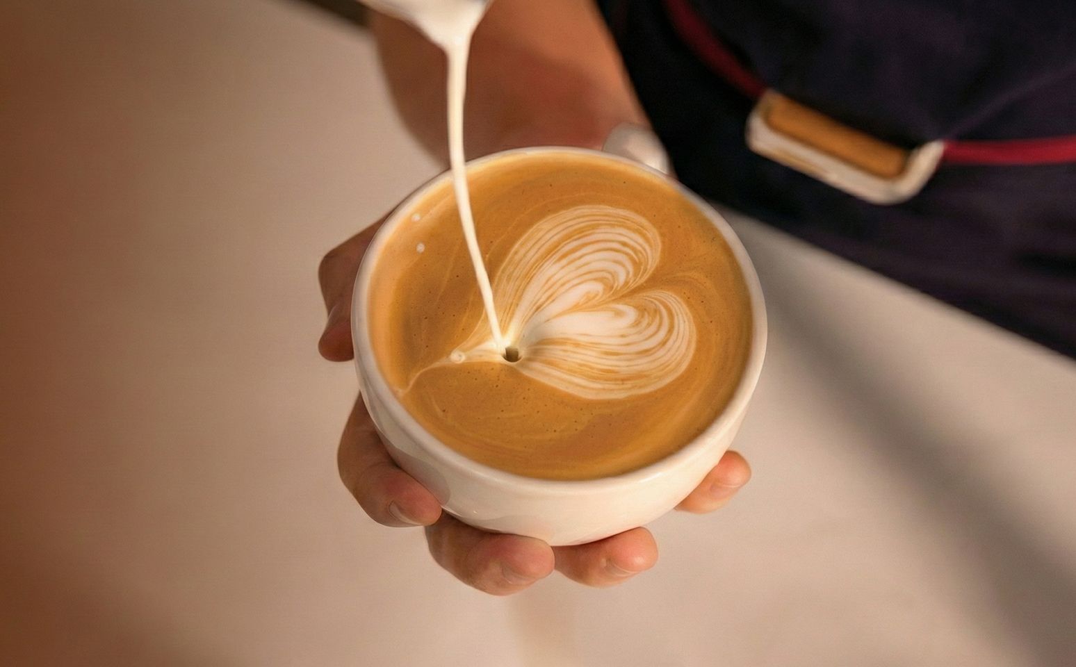 Barista pouring milk to create a heart latte art in a cappuccino cup
