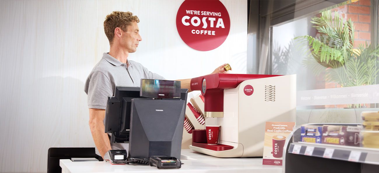 A man is making a coffee at a Costa Podio machine