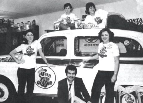 Historic black-and-white photograph showing members of the Costa team alongside a branded Costa Coffee vehicle during the company’s early years.