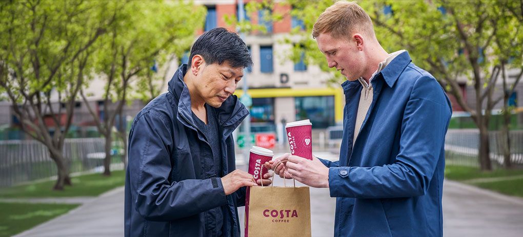 Two people drinking coffee from takeaway Costa Coffee cups during a casual outdoor meet-up.