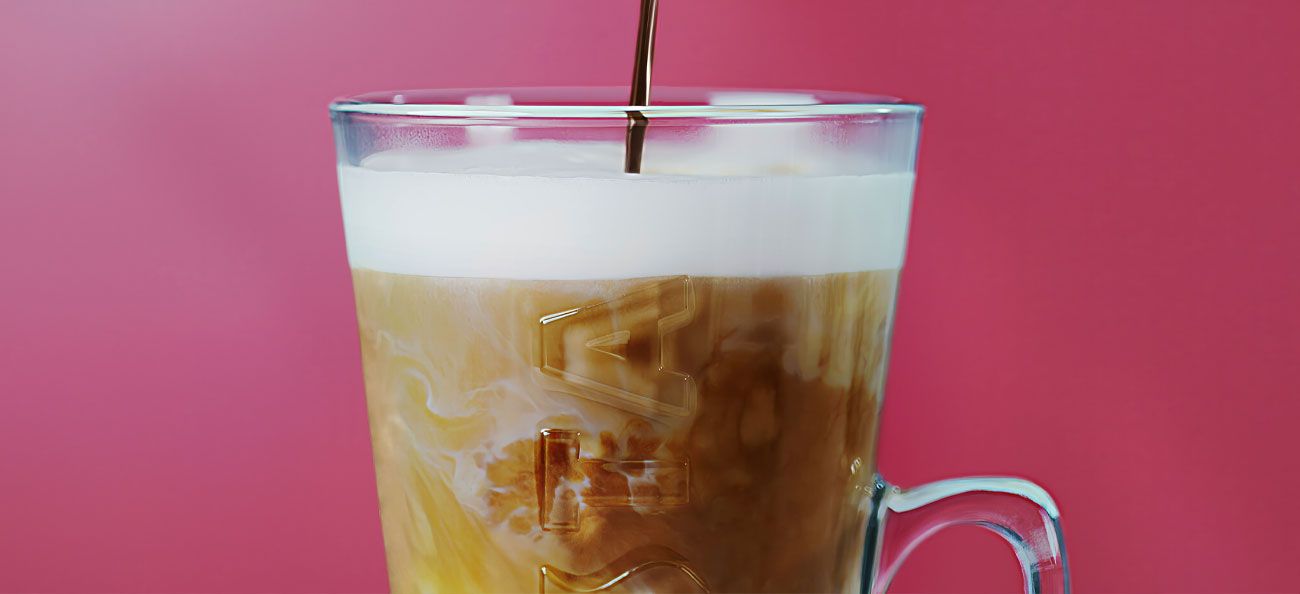Costa Coffee iced coffee in a glass mug with milk being poured in, creating swirling patterns beneath a creamy foam laye