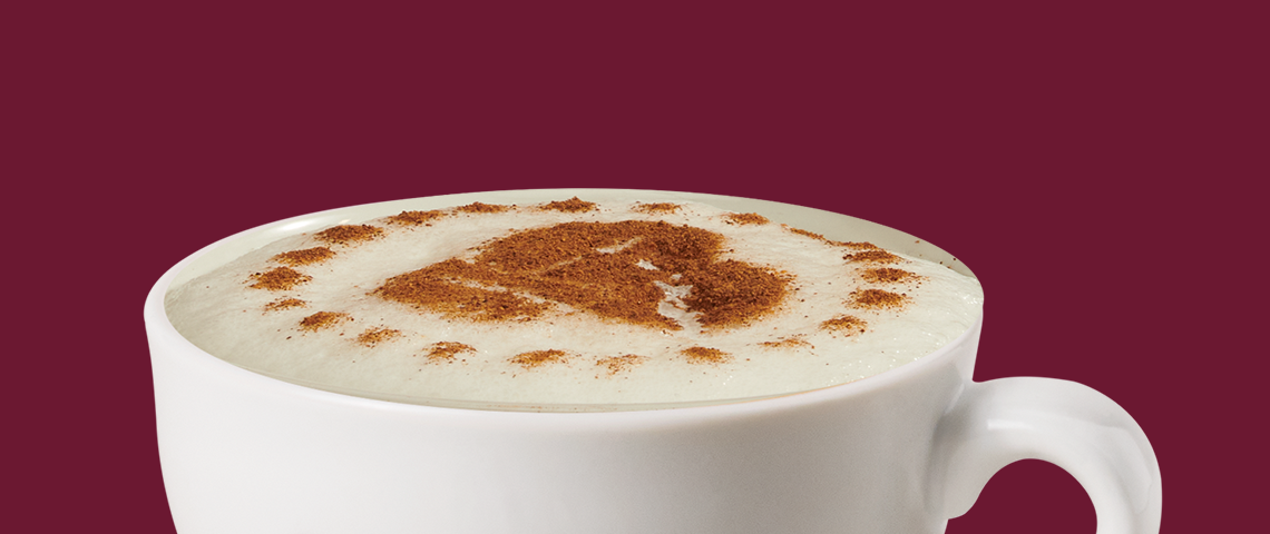Capuchino en taza blanca con espuma y arte de café con canela encima