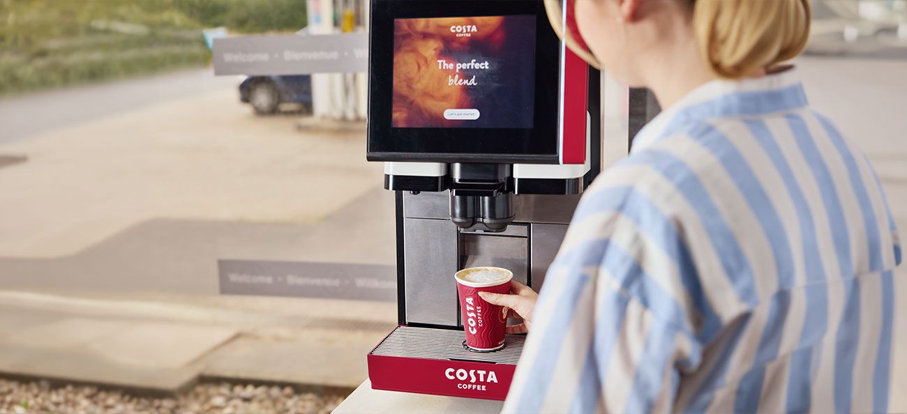 A woman is making a Costa coffee at a Costa Machine