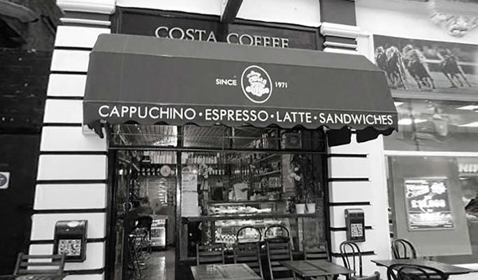 Fachada de Costa Coffee con toldo, mesas, sillas y rótulos de café desde 1971