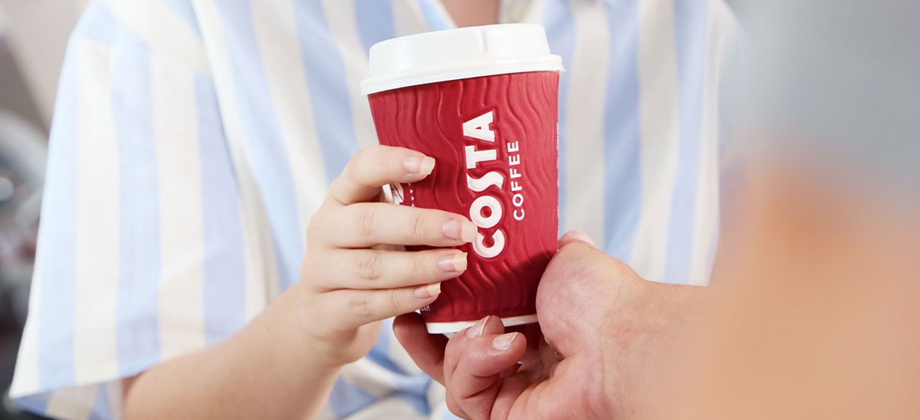 A person hands a freshly prepared Costa Coffee cup to another customer