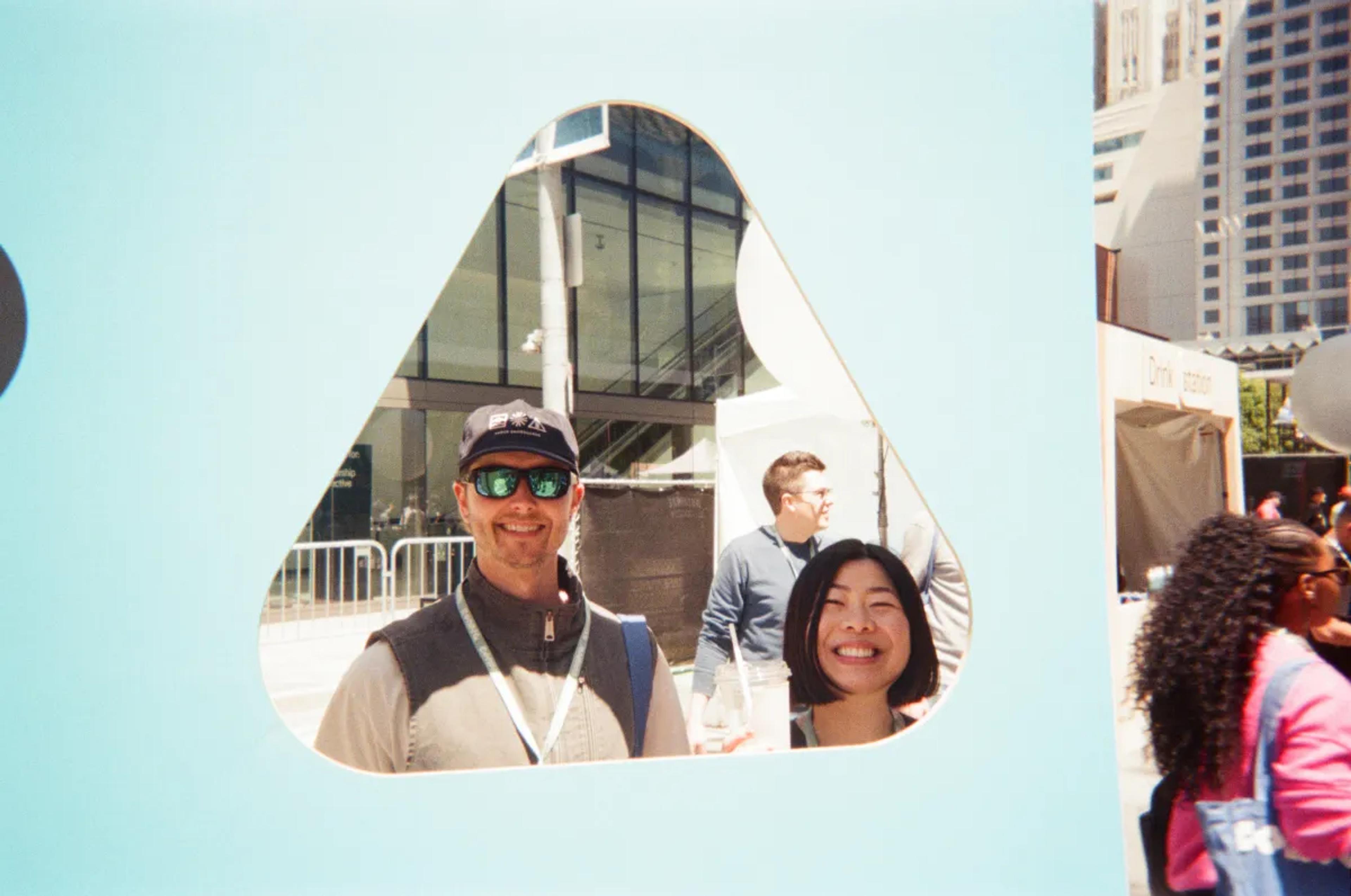 Two smiling conference attendees pose behind a teardrop-shaped cutout in a blue display.