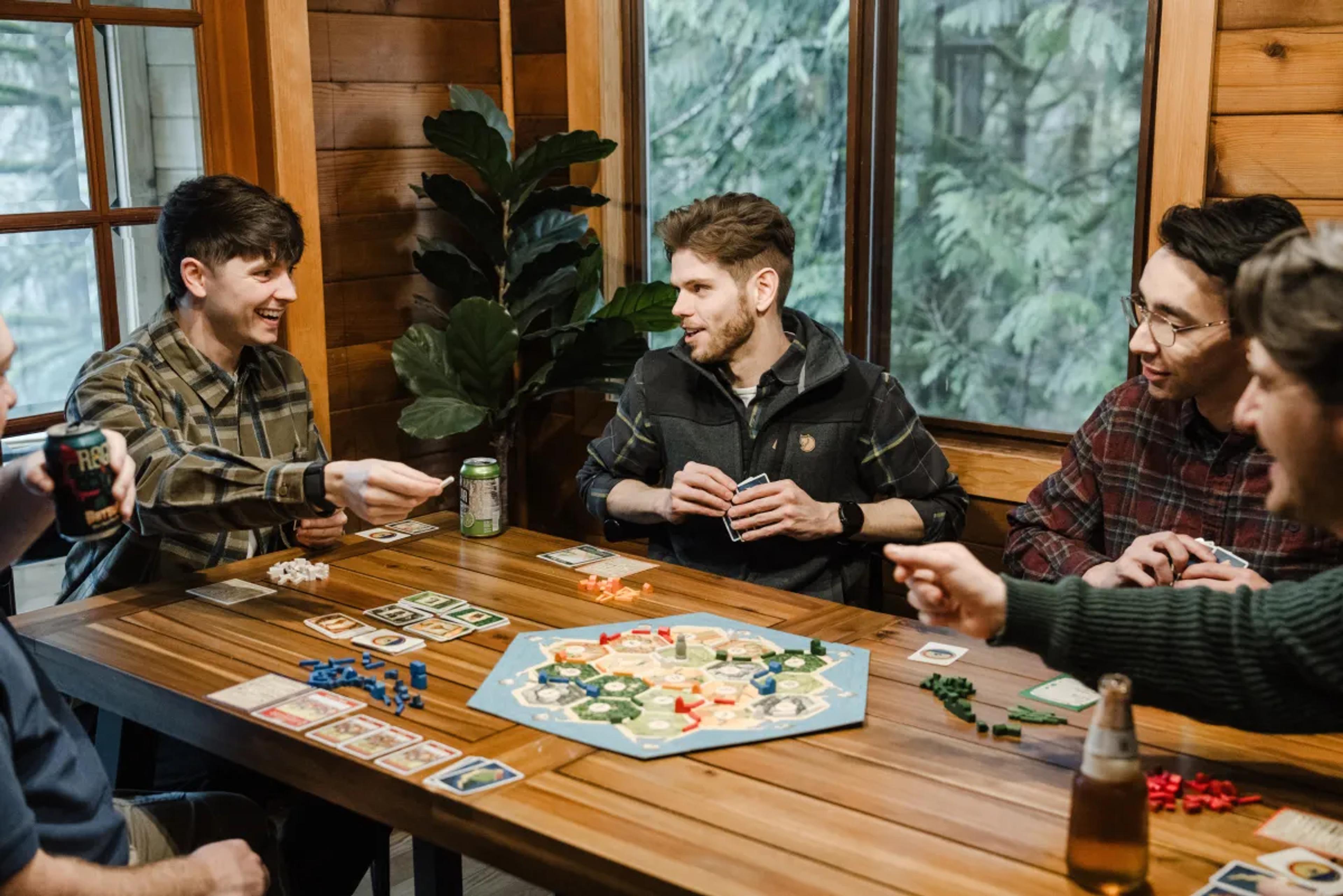 Coworkers laugh and play a board game around a wooden table in a cozy cabin.