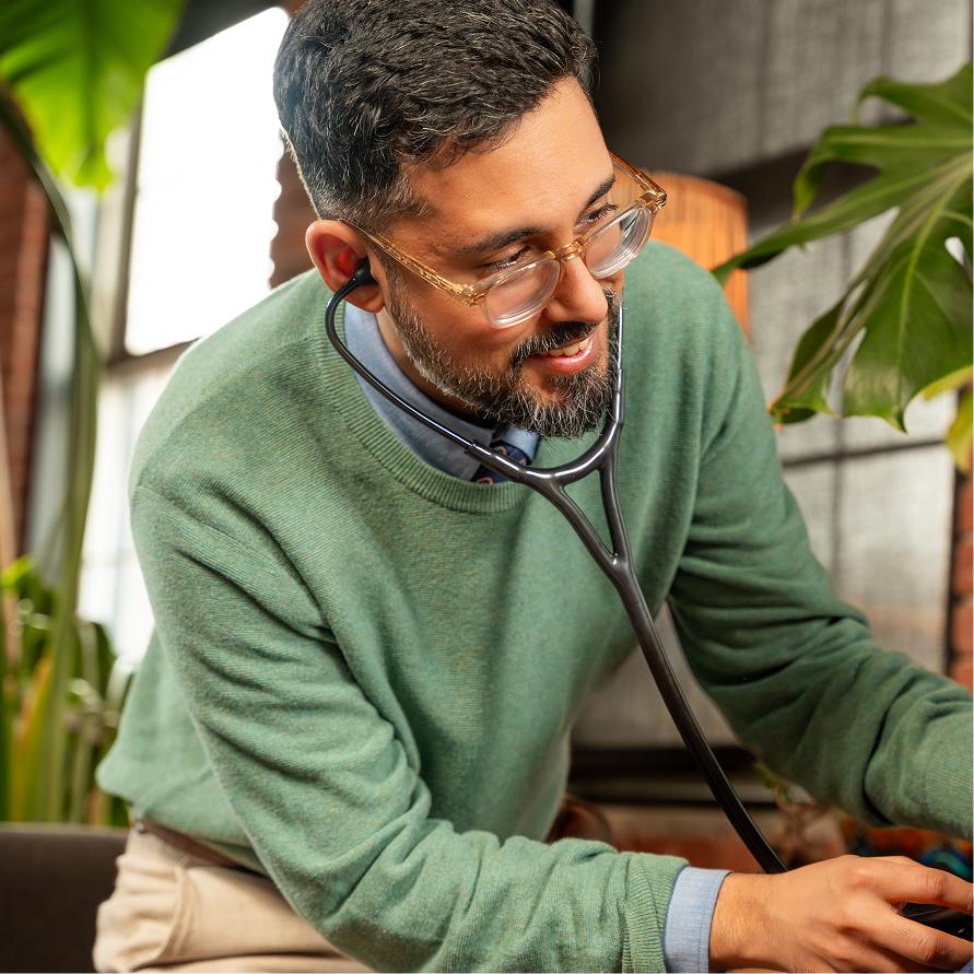 A doctor with a stethoscope working at a plant-filled desk