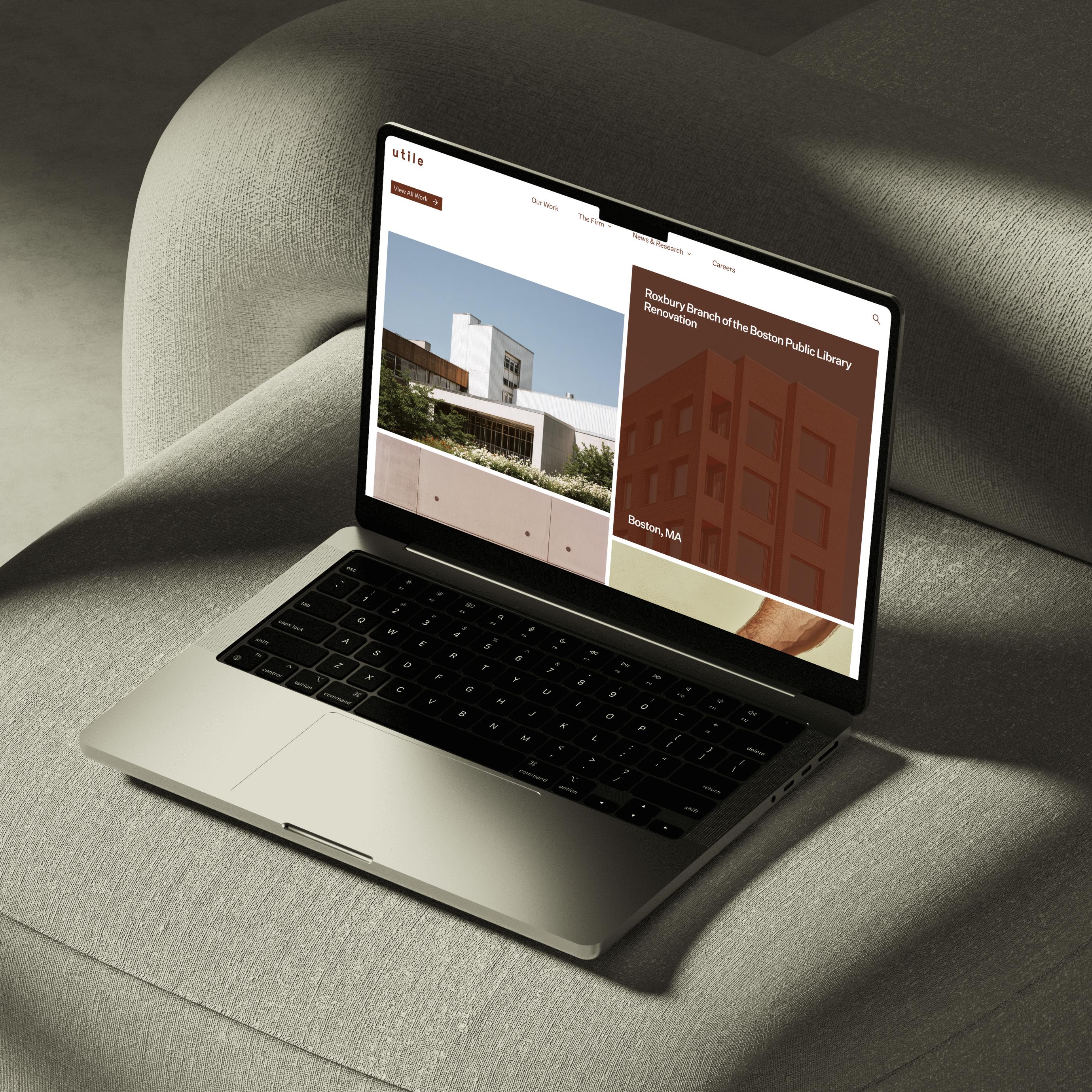 A laptop on a chair cushion displaying the Utile Design website