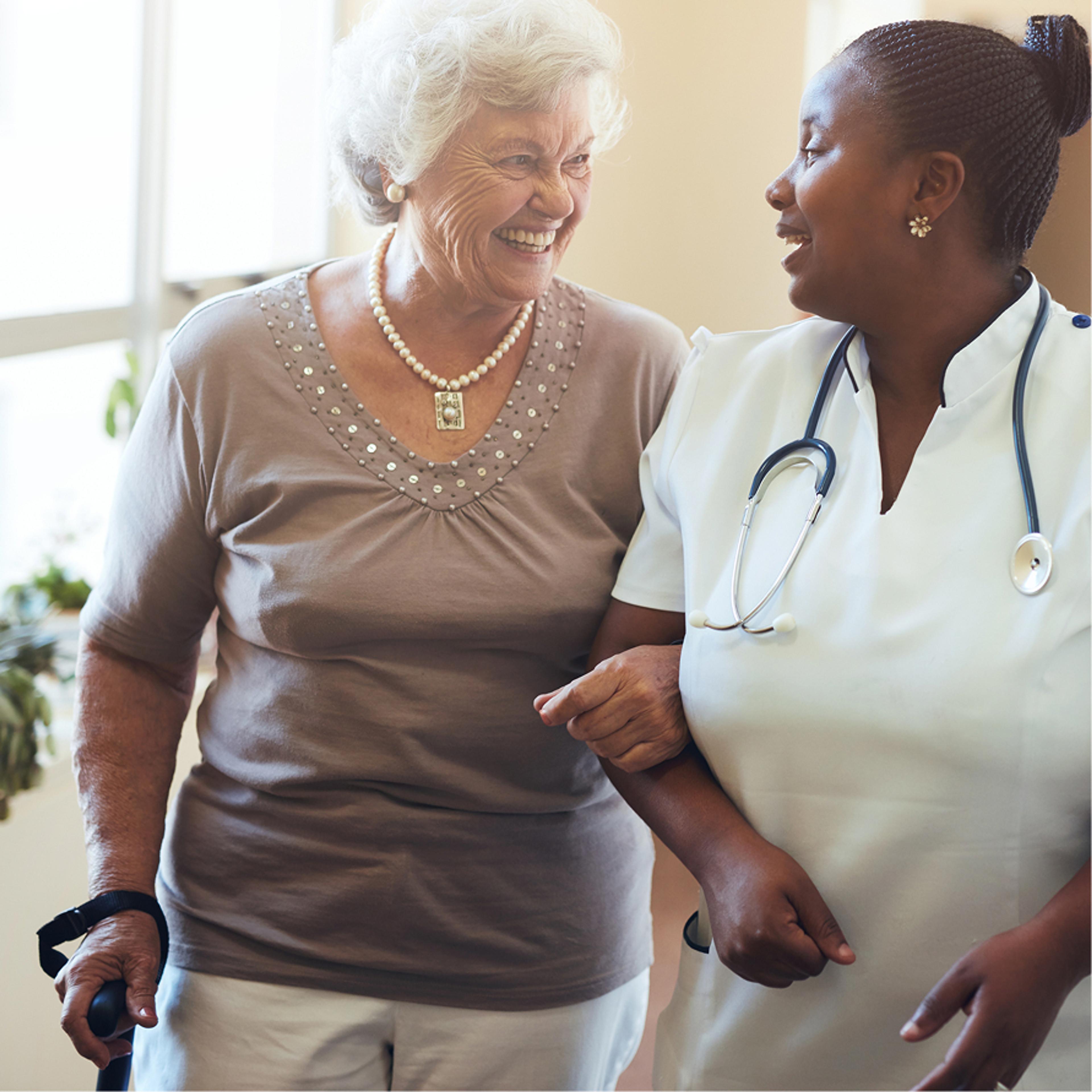 A nurse walking arm in arm with a smiling older patient