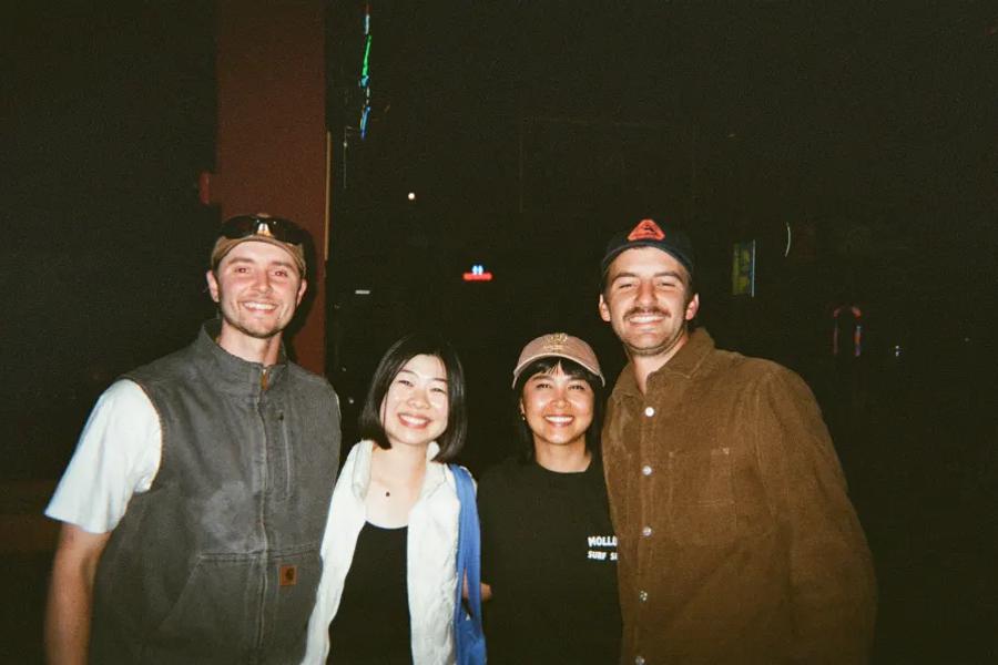 Four friends smile together at a dimly lit nighttime venue.