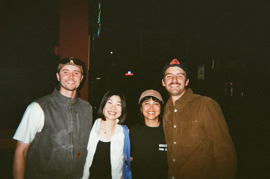 Four friends smile together at a dimly lit nighttime venue.