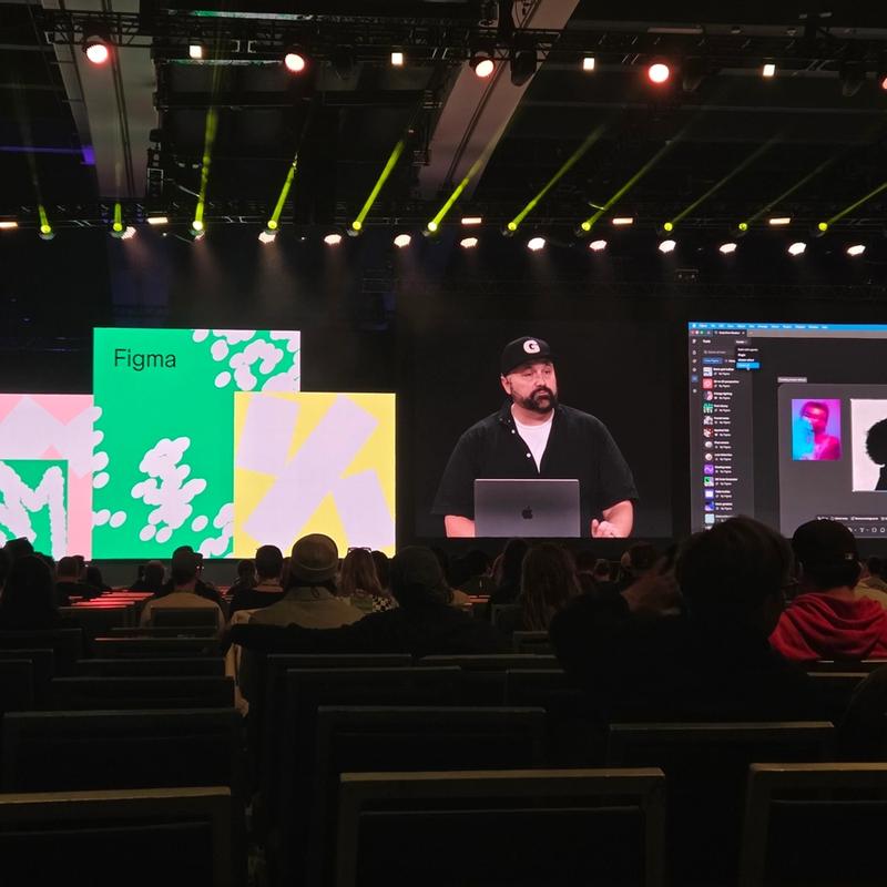 Presenter demonstrates Figma on a large screen before a seated conference audience.